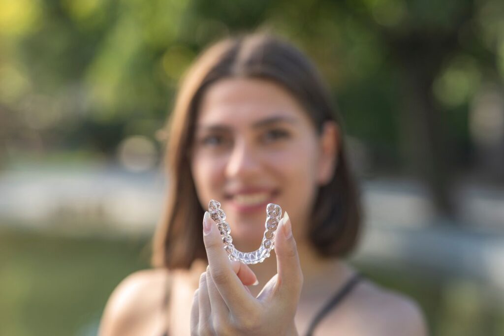 A woman with tilted smile holding Invisalign aligners