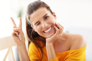 Happy woman in yellow top making peace sign and smiling, ready for dental consultation.