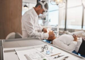 Dentist examining patient in treatment room with sterilized instruments on tray.